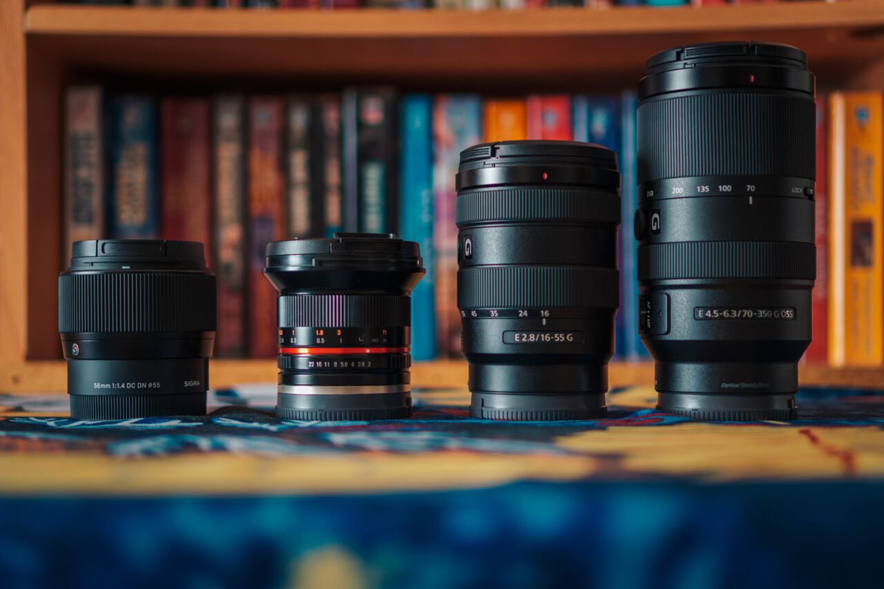 4 camera lenses lined up in front of a bookshelf