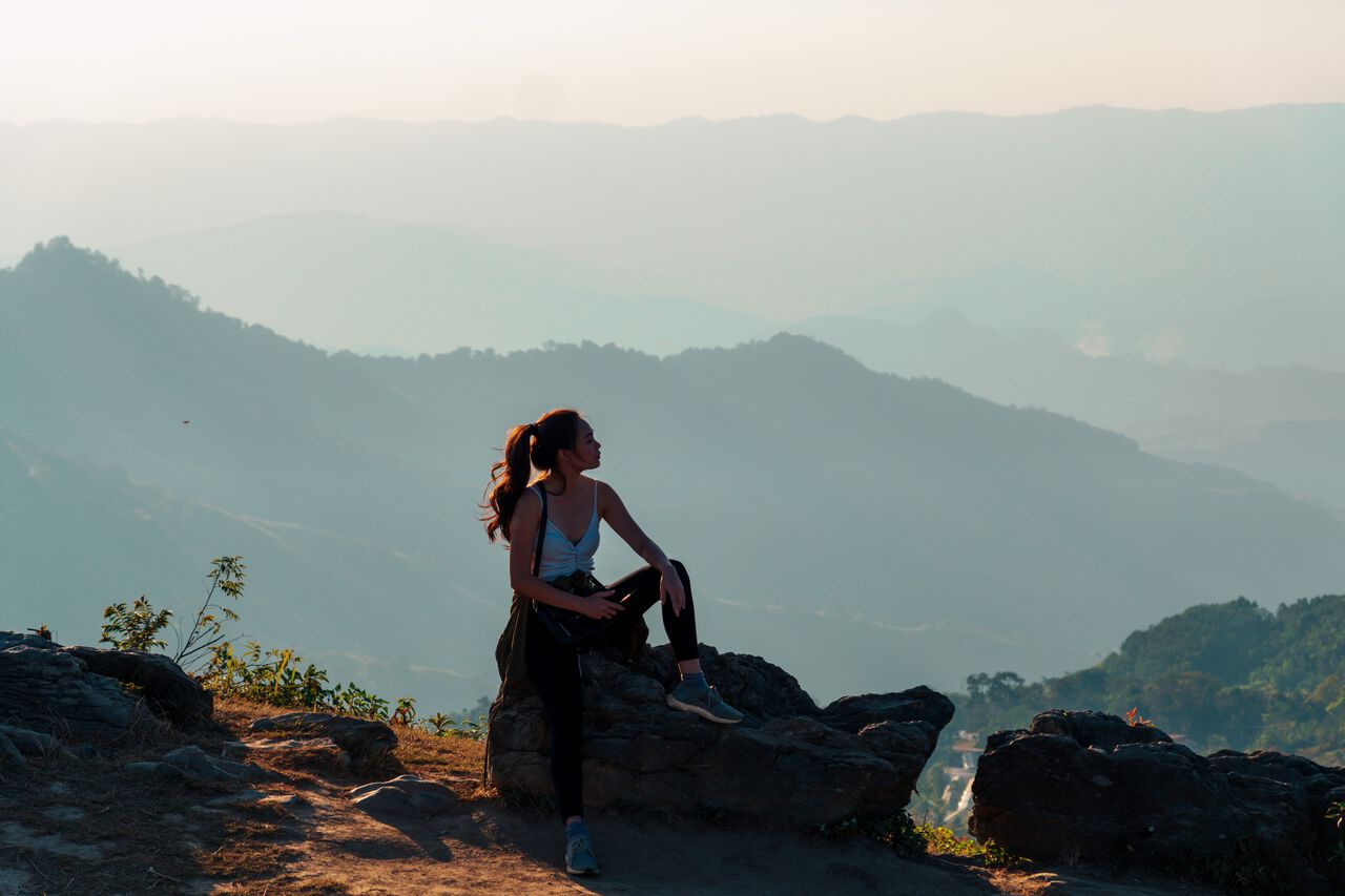 A woman sitting on a rock during sunset at Doi Pha Tang in Chiang Rai