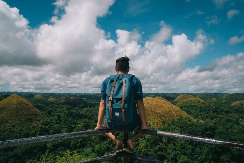 Uma pessoa com uma mochila sentado em uma montanha com vista para o Chocolate Hills, nas Filipinas