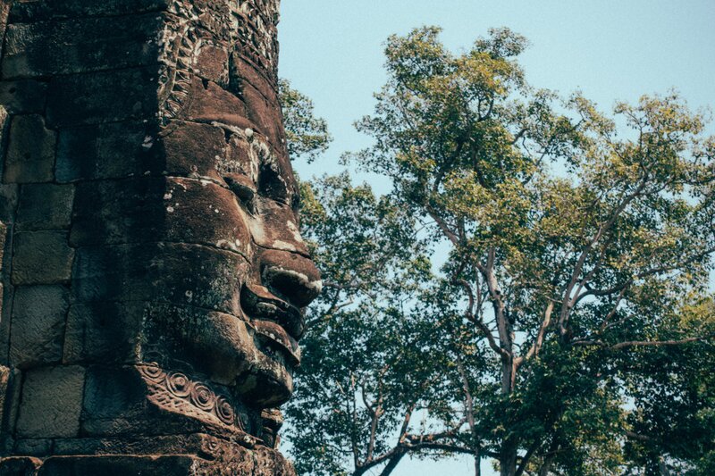 en av smiley sten ansikte Bayon temple framför en massiv träd i Angkor Wat.