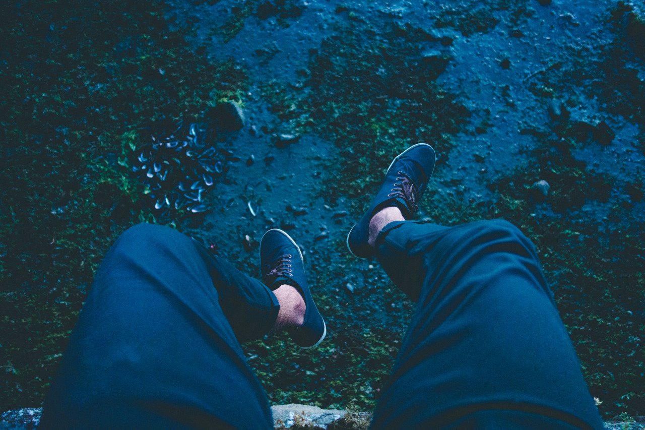A person wearing travel shoes with his legs out over a ledge on the dried up beach in New Zealand