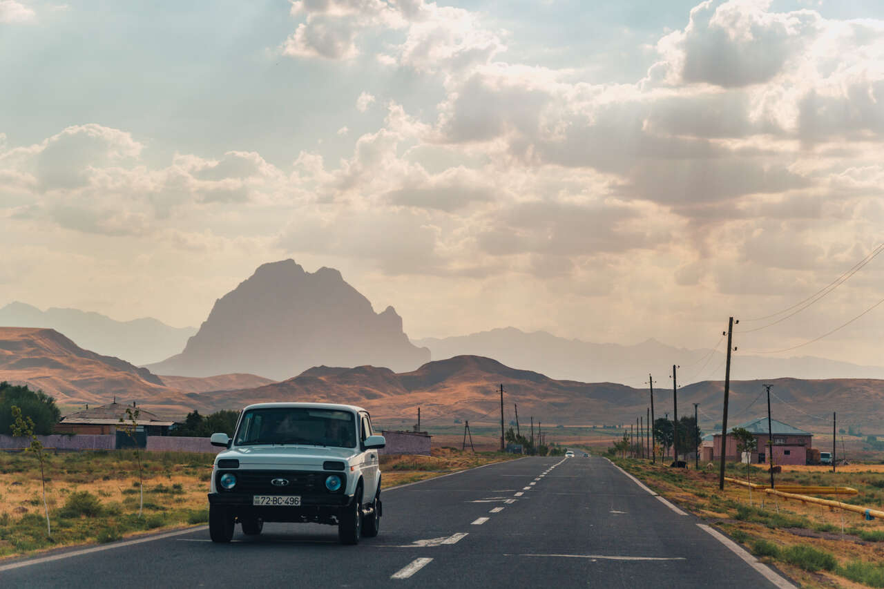 A jeep driving away from a mountain on an empty road in Nakhchivan, Azerbaijan.
