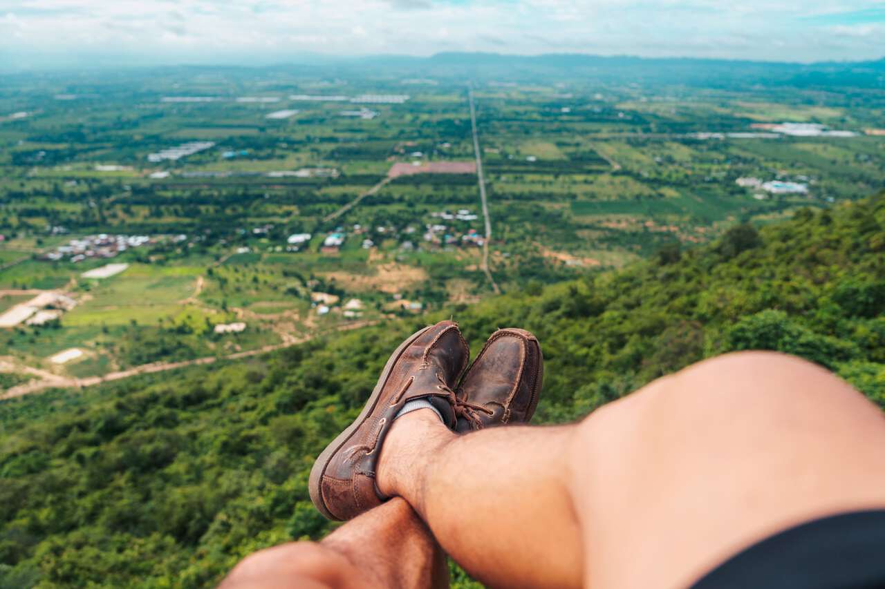 A person wearing a travel shoe with his legs off a mountain ridge in Lopburi, Thailand