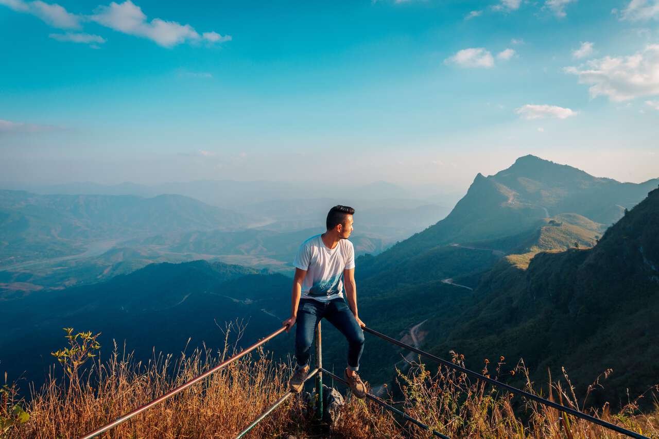 A person sitting on the ledge facing Phu Chi Fa at the top of Doi Pha Tang in Chiang Rai