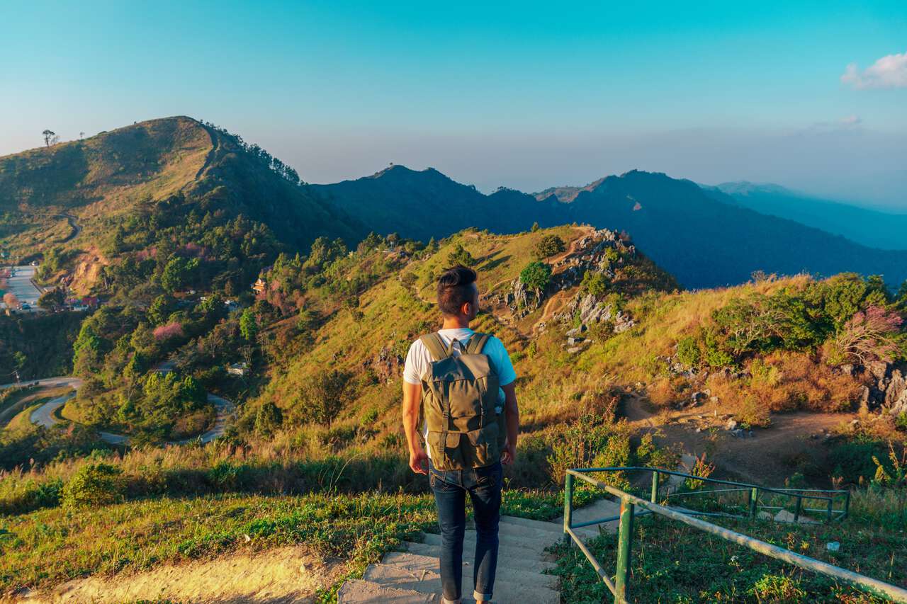 A person standing looking at the mountains during sunset at Doi Pha Tang near Phu Chi Fa, Chiang Rai