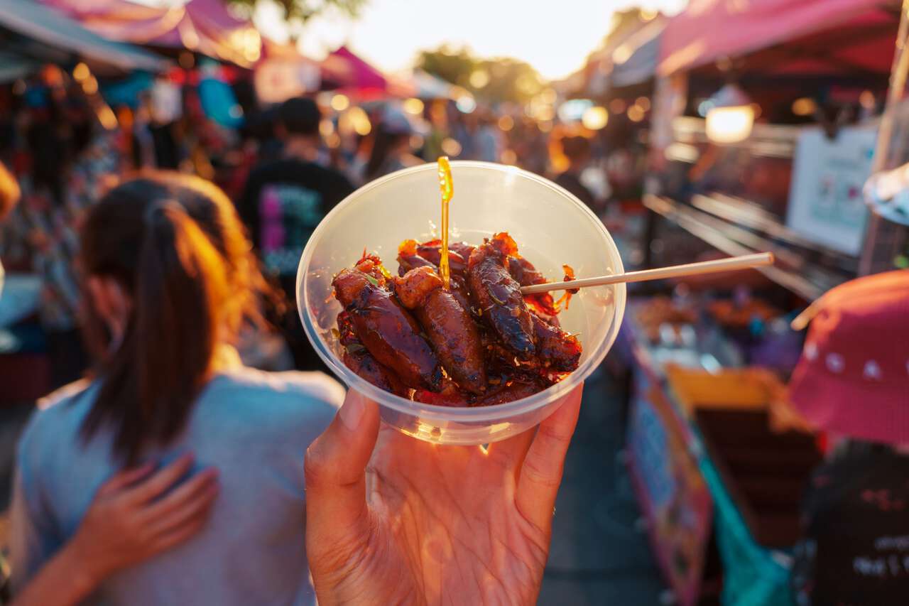 A person holding a bowl of grilled squid street food in Thailand