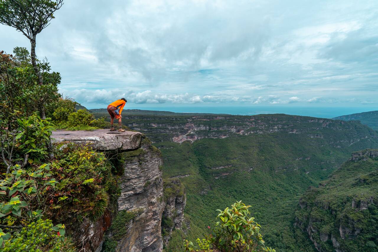 A person on the edge of a cliff looking down Cachoeira da Fumaça