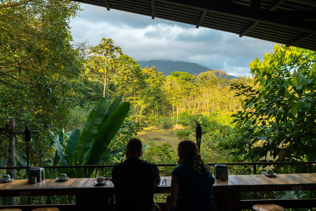 People sitting in a lodge looking at a clouded arenal volcano in costa rica