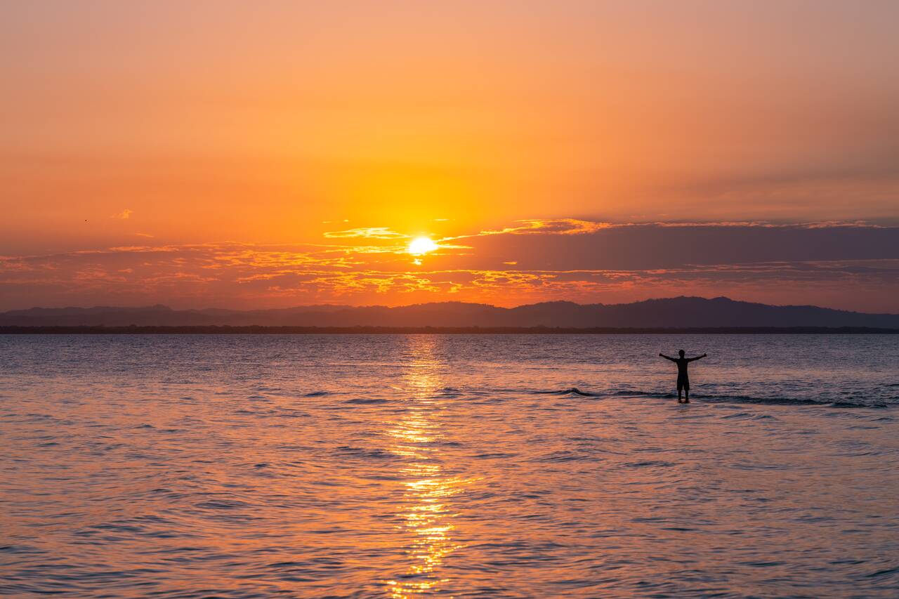 A person posing at the nanrrow sand bank at Punta Jesús María during sunset