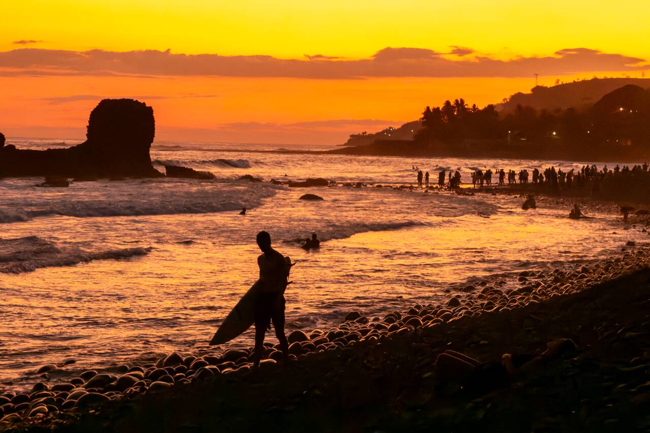 A surfer walking at El Tunco Beach at sunset