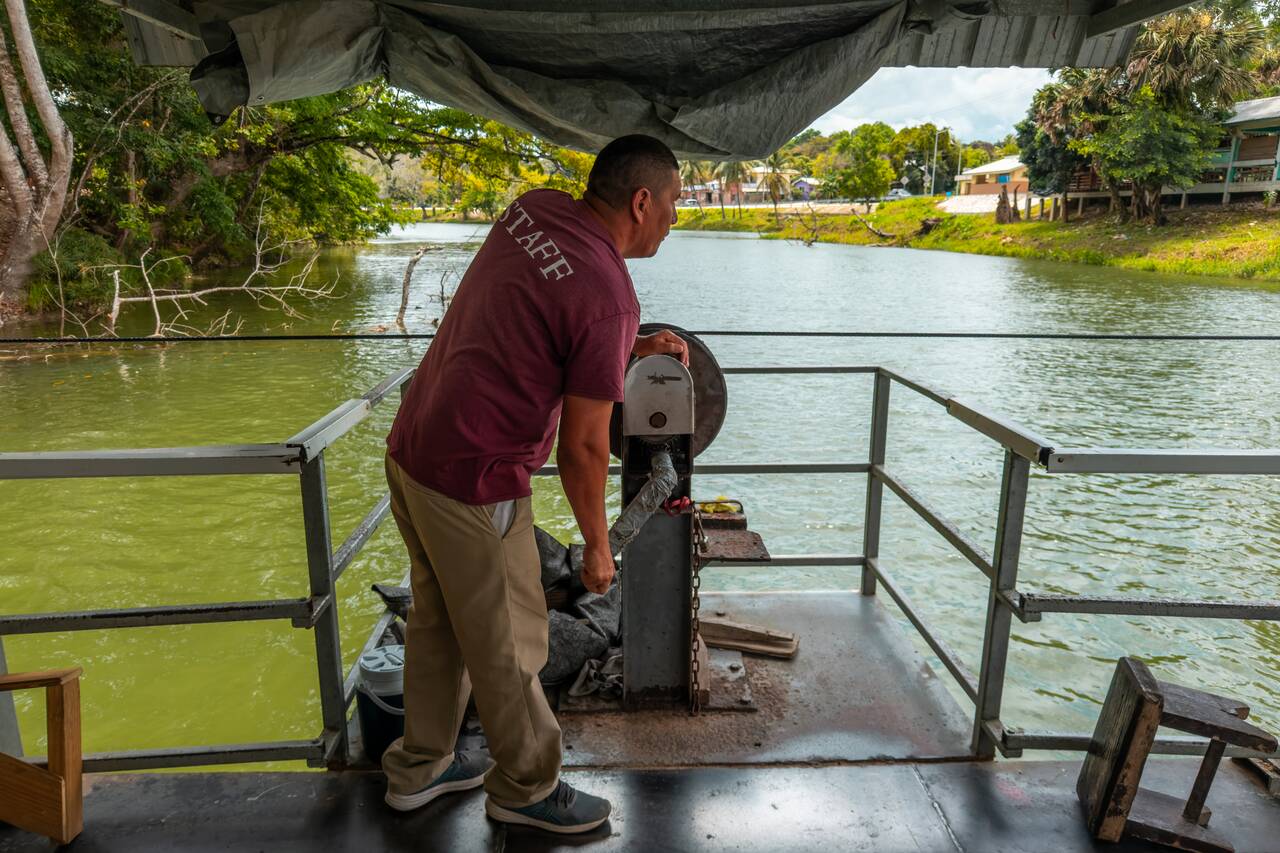A man hand cranking a ferry across the river in Benque
