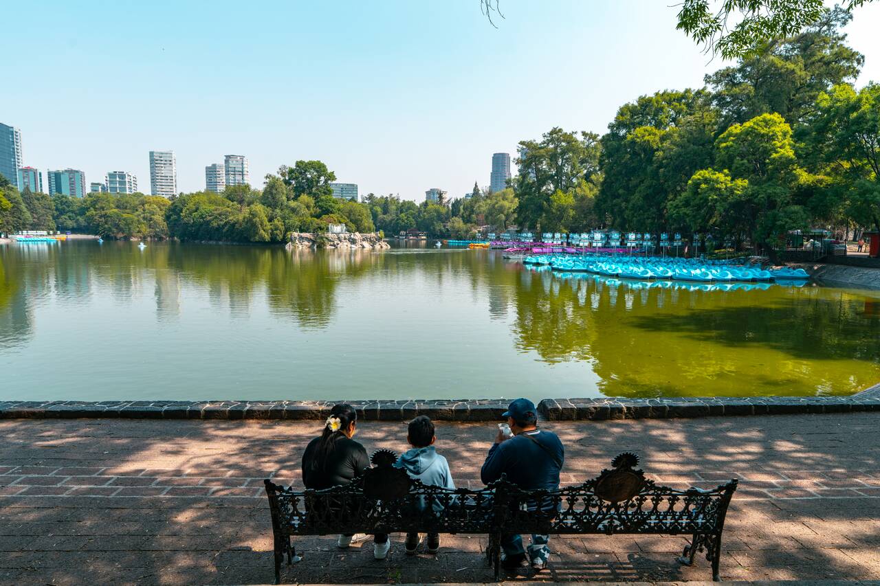 A family sitting at a bench by the lake inside Chapultepec Park