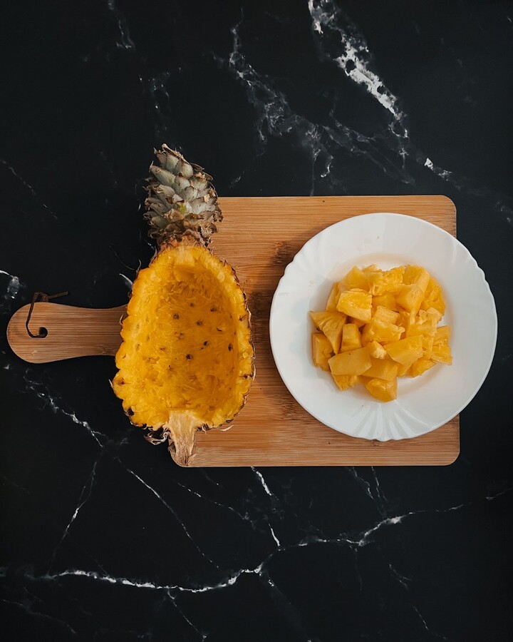 To prepare a pineapple, start by cutting it in half with a sharp knife. Then, carefully slice around the perimeter of the fruit, removing the skin. Make a horizontal cut along either side of the core, and use a spoon to scoop out the cubed fruit. Place the diced pineapple in a bowl for later use.