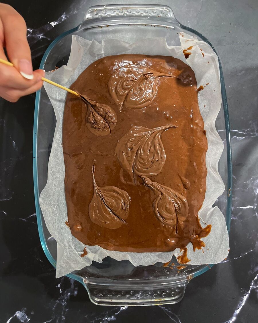 Line a baking dish or pan with parchment paper, then evenly spread the batter in it. Feel free to get creative by adding an extra layer of Nutella and using a wooden stick to create some brownie art. The possibilities are endless!