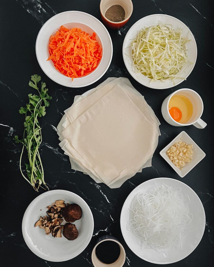 Gather all the ingredients, including grated carrots, finely-chopped shiitake mushrooms, shredded cabbage, softened glass noodles, and the required sauces.