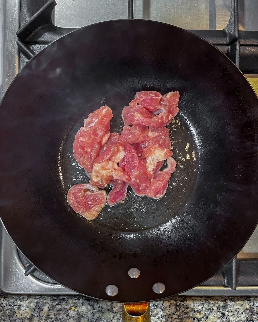Heat a wok on high and add cooking oil. Allow the wok to become very hot, then add the sliced pork. Stir the pork until it is fully cooked.