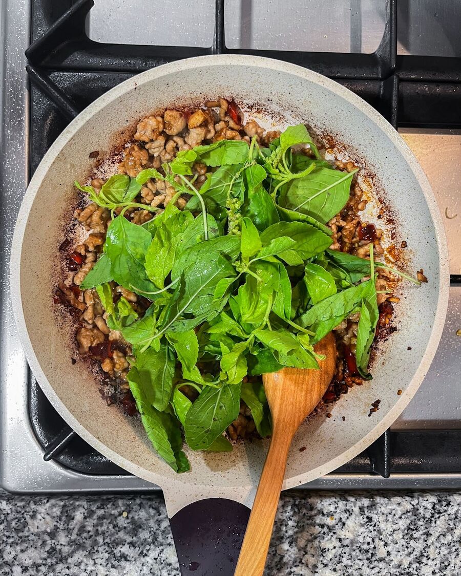 Sprinkle Thai holy basil leaves over the contents of the pan and continue to stir.