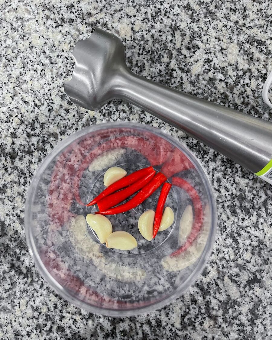 Gather all the necessary ingredients. Start by adding chilies and garlic to a food processor. Blend for a few seconds until they are finely chopped.