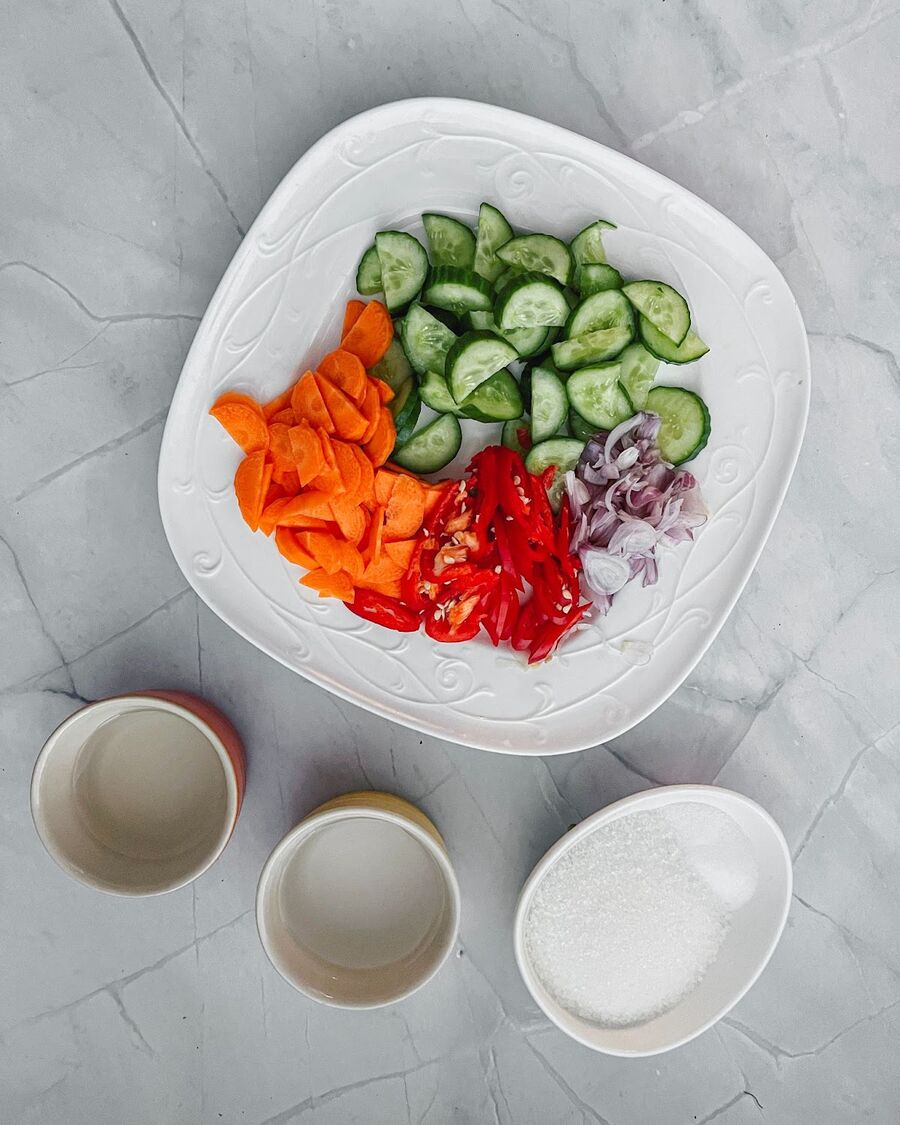 Start by gathering all the ingredients. Cut the cucumber, carrot, chili, and shallot in half and slice them..
