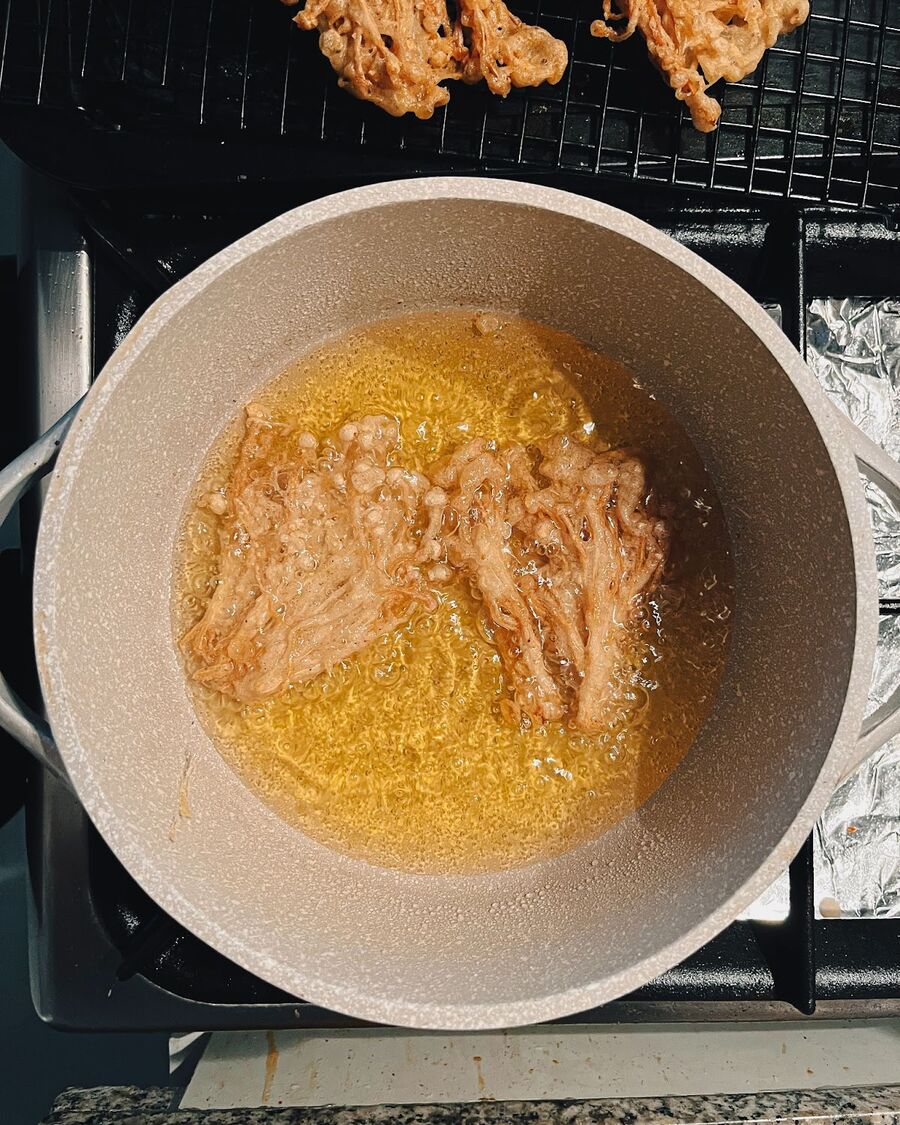 Drop the small bundles of coated Enoki mushrooms into the hot oil. Be sure not to pack the mushrooms too tightly in the pan, as this can cause them to become soggy. Add 2-3 small bundles at a time and allow them to bloom in the oil. Fry the mushrooms until the bottom side turns a golden brown color, then flip them over and fry the other side until it becomes a nice golden brown as well.