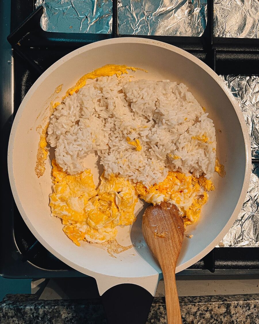 Set the scrambled eggs to the side of the pan, then add the chilled steamed rice to the other side.