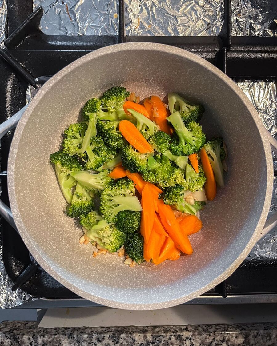 Add broccoli and carrot to the pan first. Stir them a few times, then cover the pan with a lid and let them cook for 2 minutes.