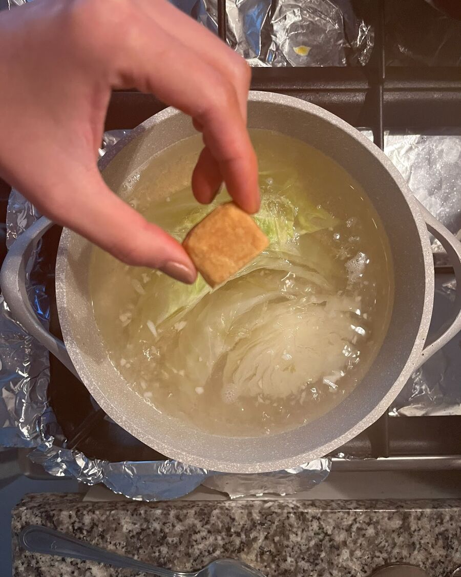 To prepare the soup, start by placing a chicken broth cube into a soup pot with water on medium-high heat. Then add 1 tablespoon of garlic and cilantro root from the food processor, soy sauce, and let it simmer for about 15 minutes or until the cabbage is cooked.