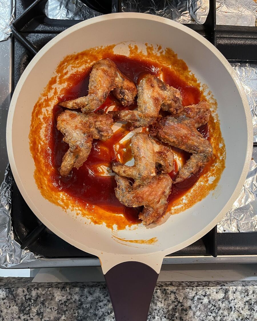 Once the wings are cooked, allow them to sit at room temperature for approximately 5 minutes to let the crispy coating set. Afterward, transfer the wings to a mixing bowl and generously coat them with the prepared sauce, ensuring each wing is well coated.