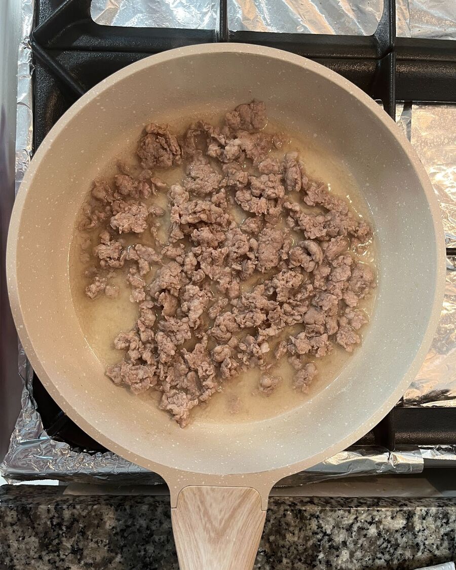 Using a skillet set to medium heat, pour in half a cup of water and allow it to come to a boil. Once it's boiling, add the ground pork and cook it until it begins to turn golden brown, which usually takes around 3 to 5 minutes.