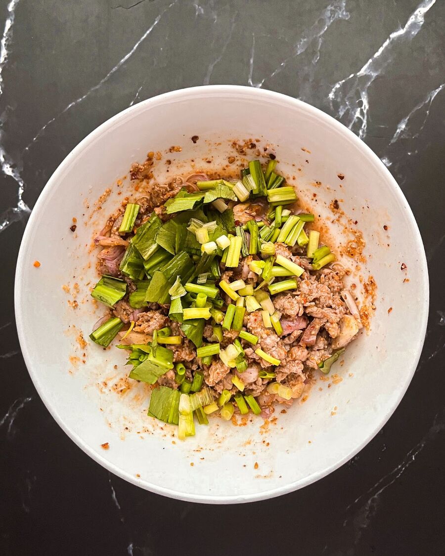 Next, include all the Thai herbs - green onions, saw leaf coriander, mint leaves - and stir them in to blend with the other ingredients.