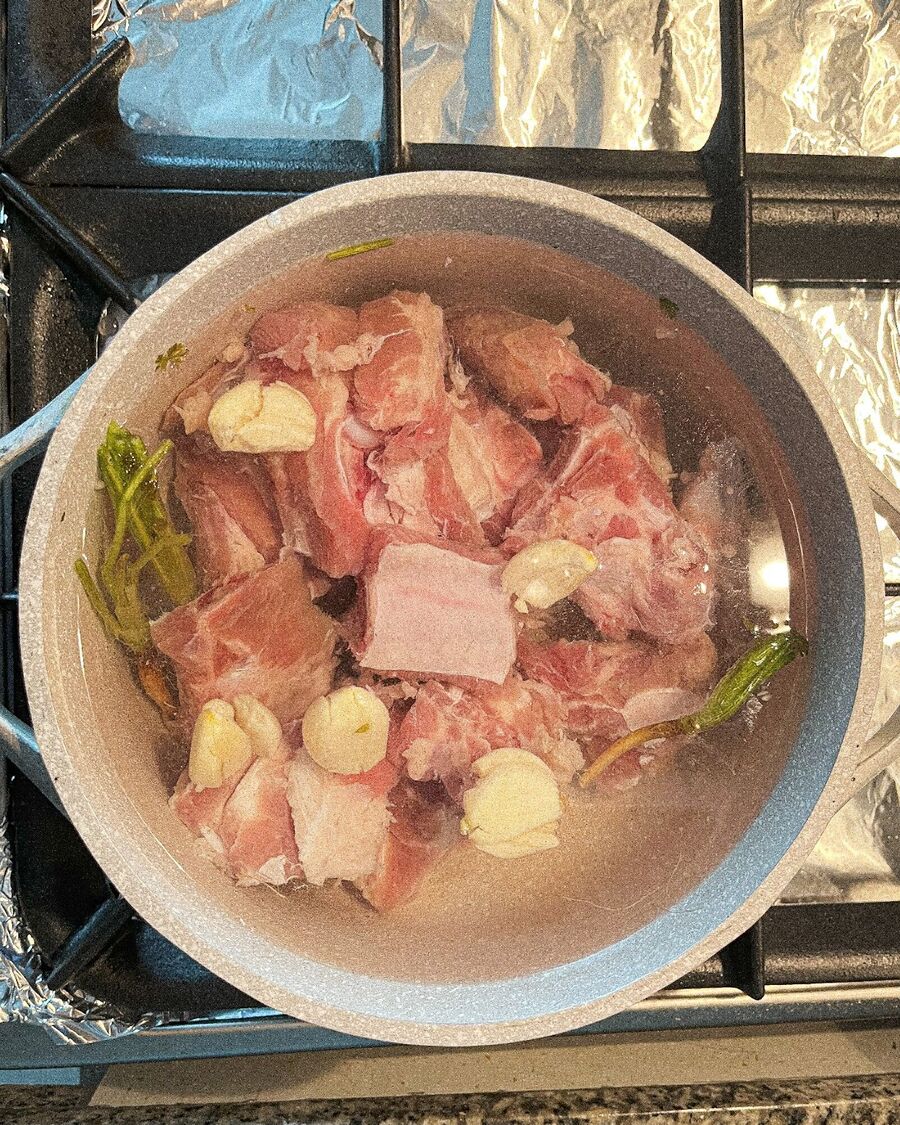 Place a soup pot over medium-high heat and add approximately 1.5 liters of water. Gently bruise the 5 garlic cloves and coriander roots, then add them to the soup pot. Introduce the spare ribs and let them cook for about 40 minutes to 1 hour.
