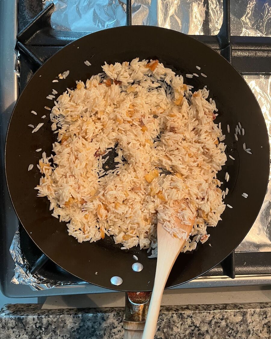 Add the uncooked Jasmine rice to the wok pan. Stir and combine the rice with the fried garlic and dry cabbage leaves. Toss and turn the rice for about 5 minutes or until the rice starts to darken and turn slightly golden.