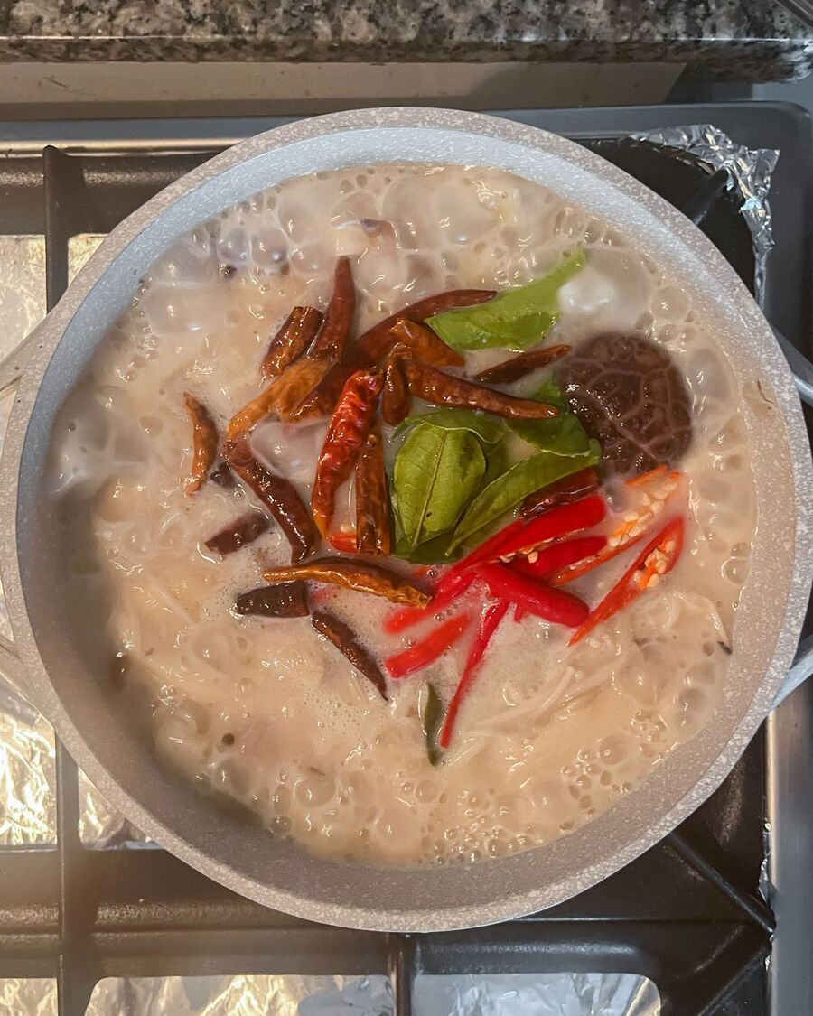 Add sliced fresh chili, roasted chili, and kaffir lime leaves over the soup, then stir to combine them.