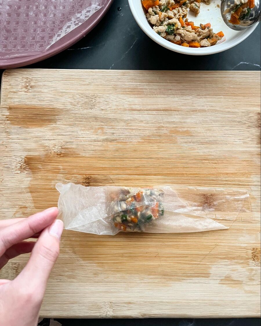 When the filling is ready and no longer hot, place a rice paper wrapper on a cutting board. Add a spoonful of the filling in the middle of the rice paper. Fold the bottom half up to cover the filling, then fold the sides in from both sides.