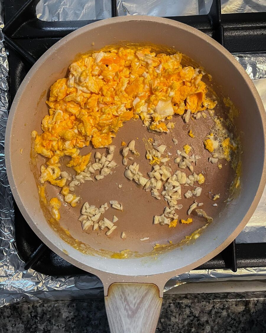 Heat cooking oil in a pan over medium-high heat. Pour the beaten eggs into the pan and scramble them. Push the scrambled eggs to one side of the pan. Add minced garlic to the empty side and stir until fragrant.