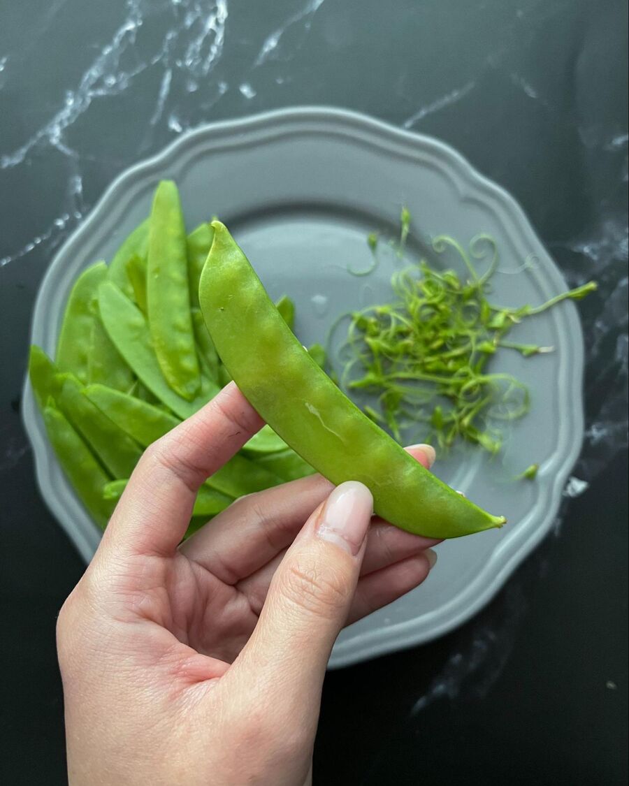 Remove the string from the snow peas by folding the stem over towards the straighter side of the snow peas. Then, pull it off along the length of the straighter side to remove both the stem and the string..