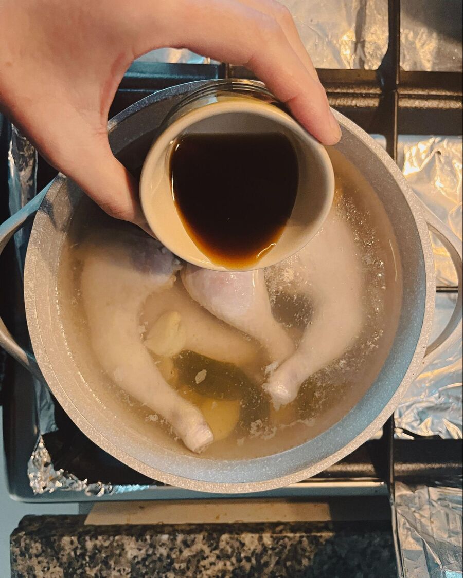Add the chicken legs to the herb-infused soup and keep the heat at a steady simmer. Stir in the fish sauce, sweet dark soy sauce, and palm sugar, ensuring the flavors blend well.